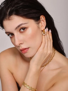 Nahaufnahme goldener Creolen mit Zirkonia-Anhängern und mehrlagigen Ketten an einem Model
