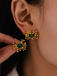 Macro shot of 18K gold plated stud earrings with deep green gemstones and radial starburst design