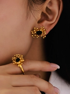 Detailed view of sunburst gold earrings and ring set with black stones on a model