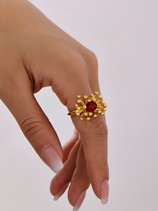Detail of a 18K gold ring with red oval gemstone and sunburst stamen design on finger