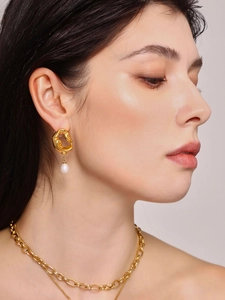 Détail de boucles d'oreilles 18k asymétriques et collier chaîne portés par un mannequin
