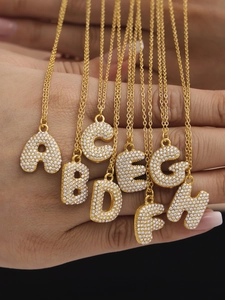 Détail macro de pendentifs lettres bulles dorés A-H sertis de zircons blancs brillants