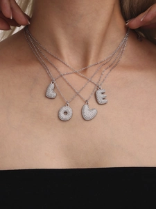 Détail de colliers argentés superposés avec pendentifs LOVE sertis de zircons