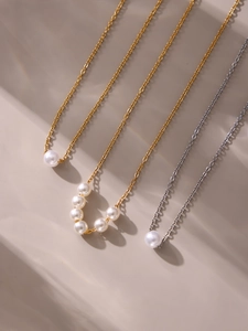 Vista dall'alto di tre collane di perle minimaliste in oro e argento su sfondo beige