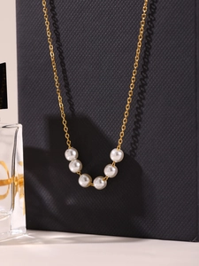 Dettaglio di un'elegante collana d'oro con sei perle bianche lucide su sfondo nero opaco