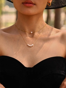 Detail view of gold layered necklaces with white pearls on a model in natural sunlight
