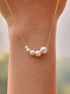 Macro detail of five graduated white pearls on a minimalist 18k gold-plated thin chain