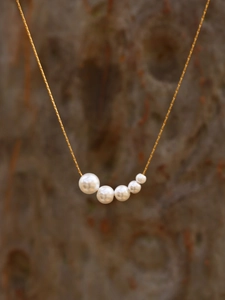 Detail of 18k gold plated necklace with five graduated white pearls in a minimalist design