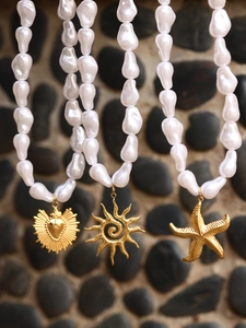 Close-up of baroque pearl necklace featuring starfish and sun charms on a pebble background