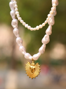 Detail of baroque pearl necklace with golden sacred heart pendant on double chain