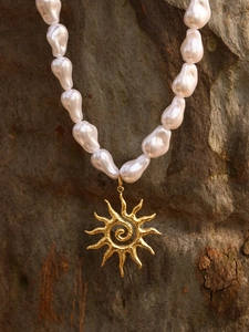 Macro detail of baroque pearls and golden sun pendant with spiral texture on rocky background