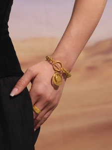 Macro detail of gold-plated OT buckle chain bracelet with relief coin pendant and wide ring