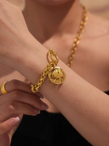Detail of OT buckle gold chain bracelet with engraved coin pendant and woven ring