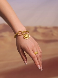 Detail of gold OT buckle chain bracelet with coin pendant and embossed wide band ring