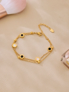 Makro-Detail des goldenen zweilagigen Armbands mit schwarz-weißen runden Anhängern
