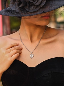 Gros plan d'un collier pendentif cœur gravé porté par un mannequin élégant en noir