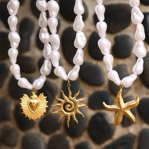 Baroque pearl necklaces featuring golden heart, sun, and starfish pendants on stones