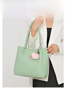 Détail d'un sac cabas vert clair texturé avec anses tressées et breloque pêche