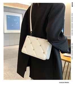Detailed view of white quilted crossbody bag with gold studs on a model's shoulder
