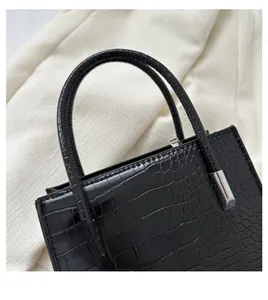 Detail of black crocodile texture handbag with padded round handle and silver metal accents