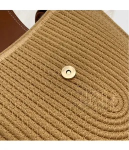 Detail of woven straw shoulder bag featuring a circular gold magnetic closure and leather trim