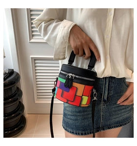 Close-up of colorful geometric patchwork cylinder bag with black handles and silver hardware