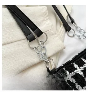 Detail of silver metal hardware and black leather strap on a black and white tweed bag