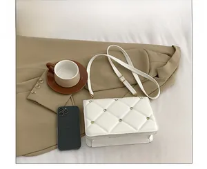 Close-up of white quilted leather bag with rhinestone rivets on a textured background