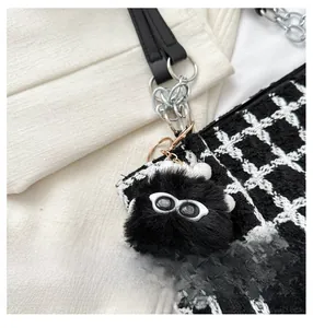 Close-up of black furry monster doll charm on a black and white tweed bucket bag