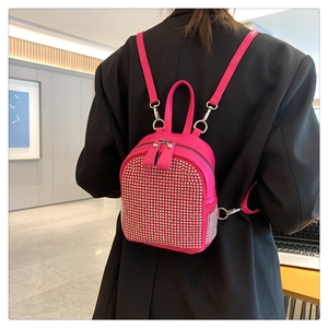 Hot pink mini backpack with silver studs shown on model in a modern indoor setting