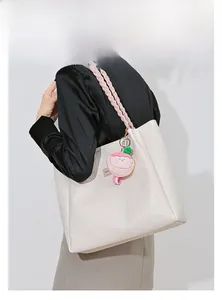 Détail d'un sac cabas en cuir crème avec anse tressée rose et breloque peluche