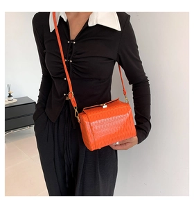 Détail du sac cylindrique orange avec texture plissée et fermoir en métal doré brillant