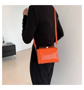 Détail du sac cylindre orange vif avec texture ondulée et finitions métalliques dorées