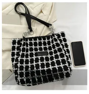 Detail view of black and white tweed tote bag with metal chain link handles and leather patch