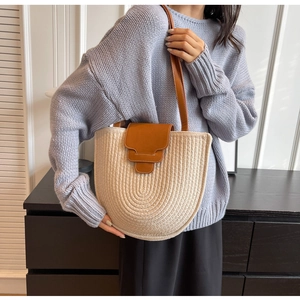 Detail of beige woven tote bag featuring brown leather flap and stylish shoulder strap