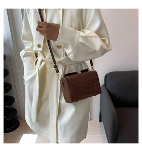 Détail d'un sac bandoulière marron à texture tressée sur un mannequin en trench