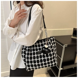 Detail view of black and white checkered tweed tote bag with a plush charm accessory