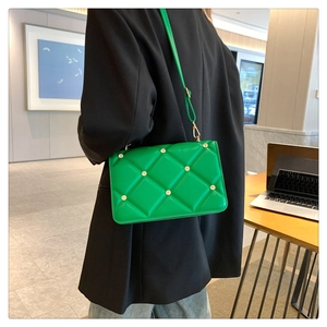 Detail of vibrant green quilted crossbody bag with gold studs and slender leather strap