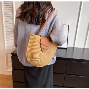 Detail showing u-shaped beige woven bag with brown leather flap and shoulder strap