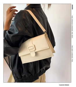 Close-up of cream leather shoulder bag with a square buckle on a black jacket
