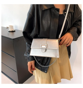 Close-up of a silver patent leather crossbody bag with large square buckle detail