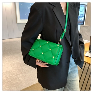 Close-up of vibrant green quilted crossbody bag with gold rivets on model's black blazer