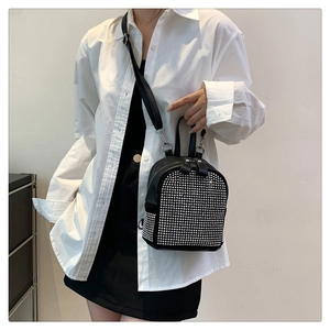 Detail of black mini backpack with silver rivets worn by a model on white shirt
