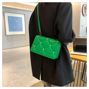 Detail view of bright green quilted crossbody bag with metal rivets on black blazer