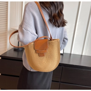 Detail of hand-woven khaki bucket bag featuring dark brown leather flap and slim strap