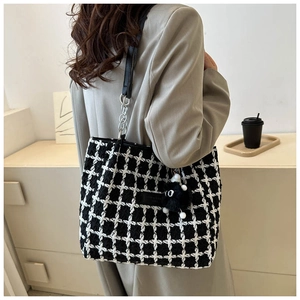 Detail of checkered tote bag with plush charm and chain strap shown on a model