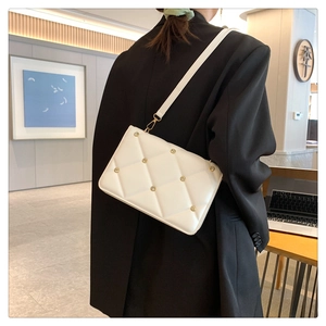 Detail of white quilted crossbody bag with rivets styled on a black blazer jacket