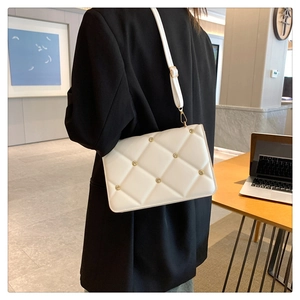 Detailed view of white quilted crossbody bag with gold studs on a model outdoors