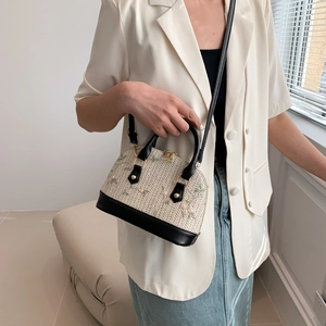 Beige straw shell handbag with pink floral embroidery and black leather straps in use