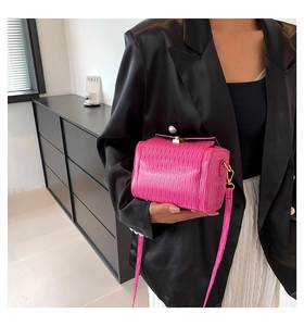 Détail du sac cylindrique plissé rose vif avec fermoir doré sur un blazer en cuir noir